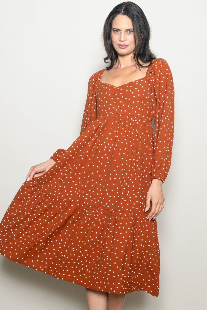 woman wearing an orange polka dot long sleeve midi dress with a square neckline and tiered skirt