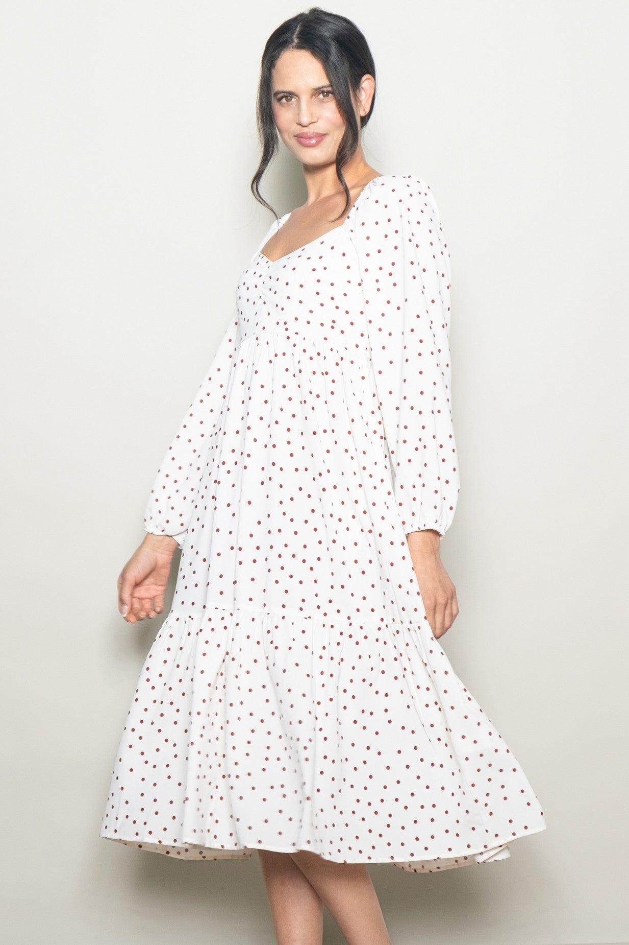 woman wearing a white midi dress with red polka dots and puff sleeves, smiling at the camera