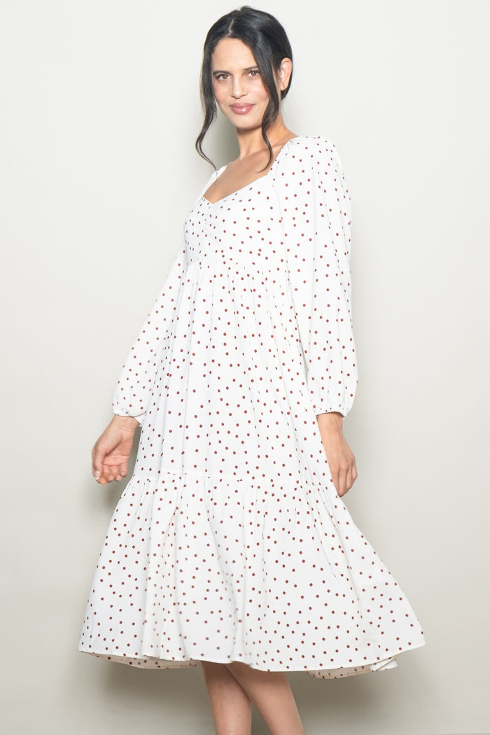 woman wearing a white midi dress with red polka dots and puff sleeves, smiling at the camera