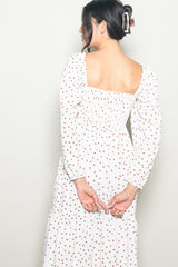 woman wearing a white long sleeve dress with red polka dots and a smocked bodice, seen from the back