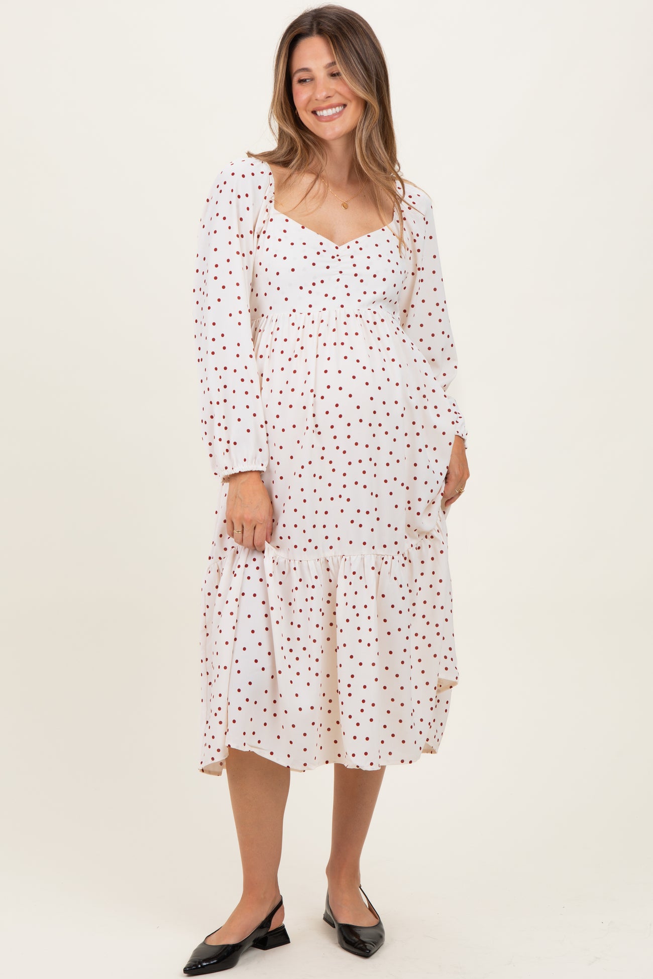 woman wearing a white maternity dress with red polka dots and a tiered hem, displaying her baby bump
