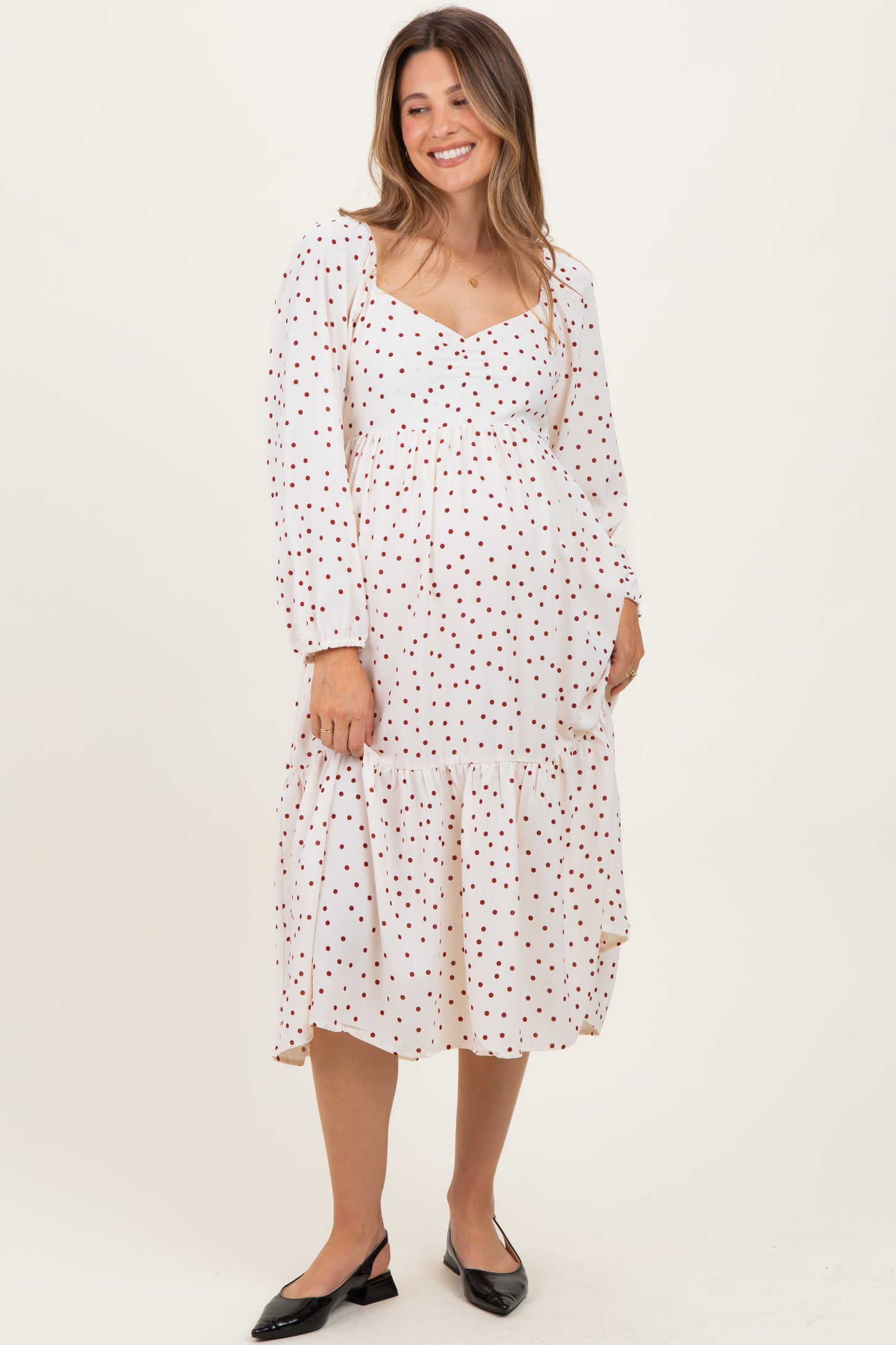 woman wearing a white maternity dress with red polka dots and a tiered hem, displaying her baby bump