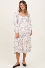 woman wearing a white maternity dress with red polka dots and a tiered hem, displaying her baby bump