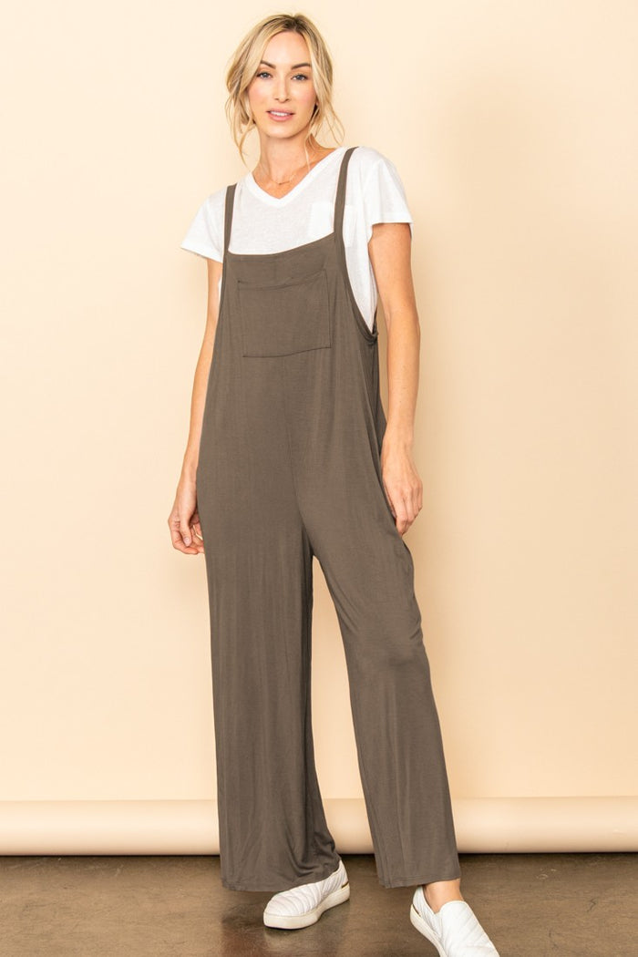 woman wearing a brown sleeveless jumpsuit over a white t-shirt with a front pocket and white sneakers
