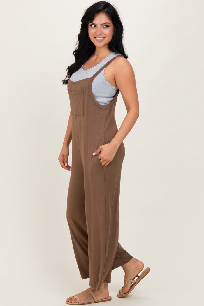 woman wearing a brown sleeveless jumpsuit over a gray tank top, standing sideways with long wavy hair