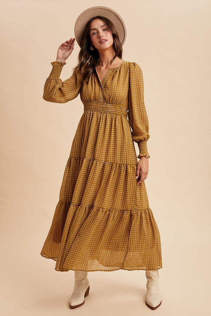 woman wearing a mustard yellow long sleeve maxi dress with tiered detailing and a smocked waist, paired with a wide-brimmed hat and ankle boots