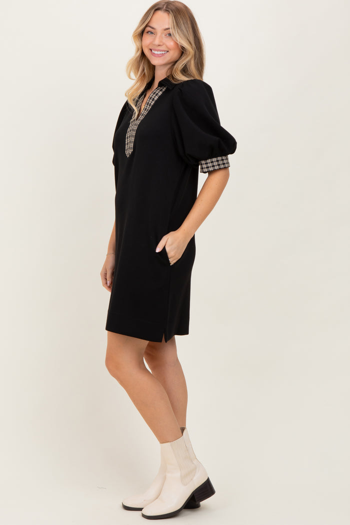 woman wearing a black short puff sleeve dress with checkered detailing and side pockets, paired with white ankle boots