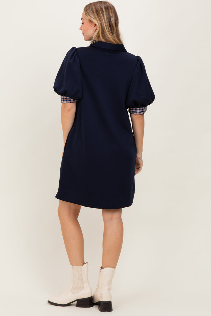 woman wearing a navy blue dress with puff sleeves and plaid details, viewed from the back, paired with white ankle boots