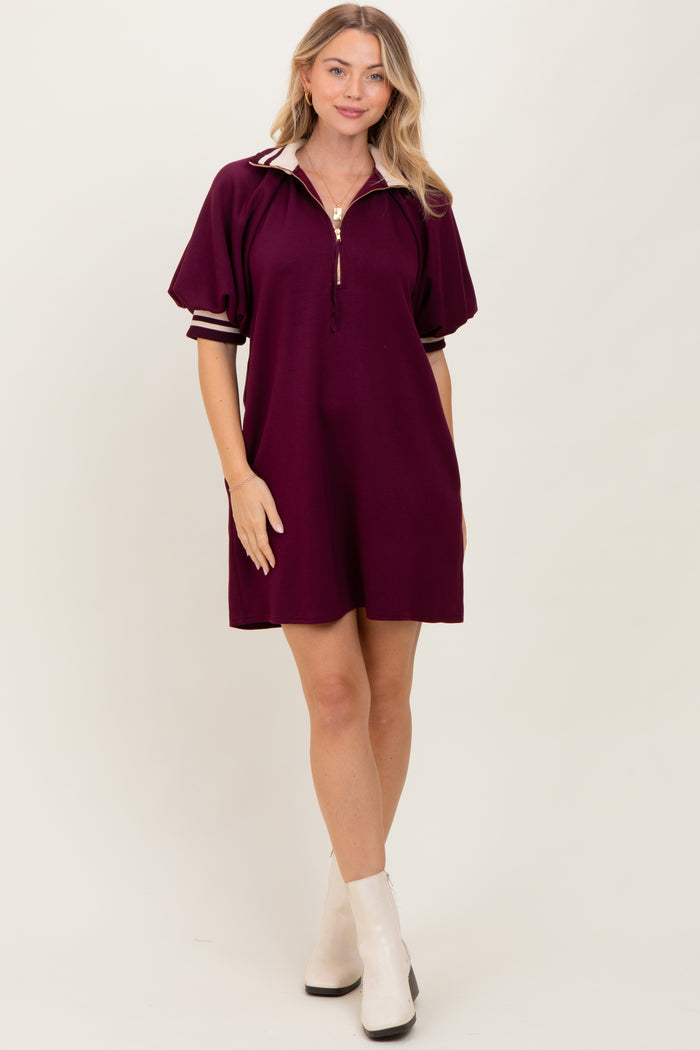 woman wearing a burgundy short sleeve polo dress with a zip neck and white striped details, standing with hands on hips