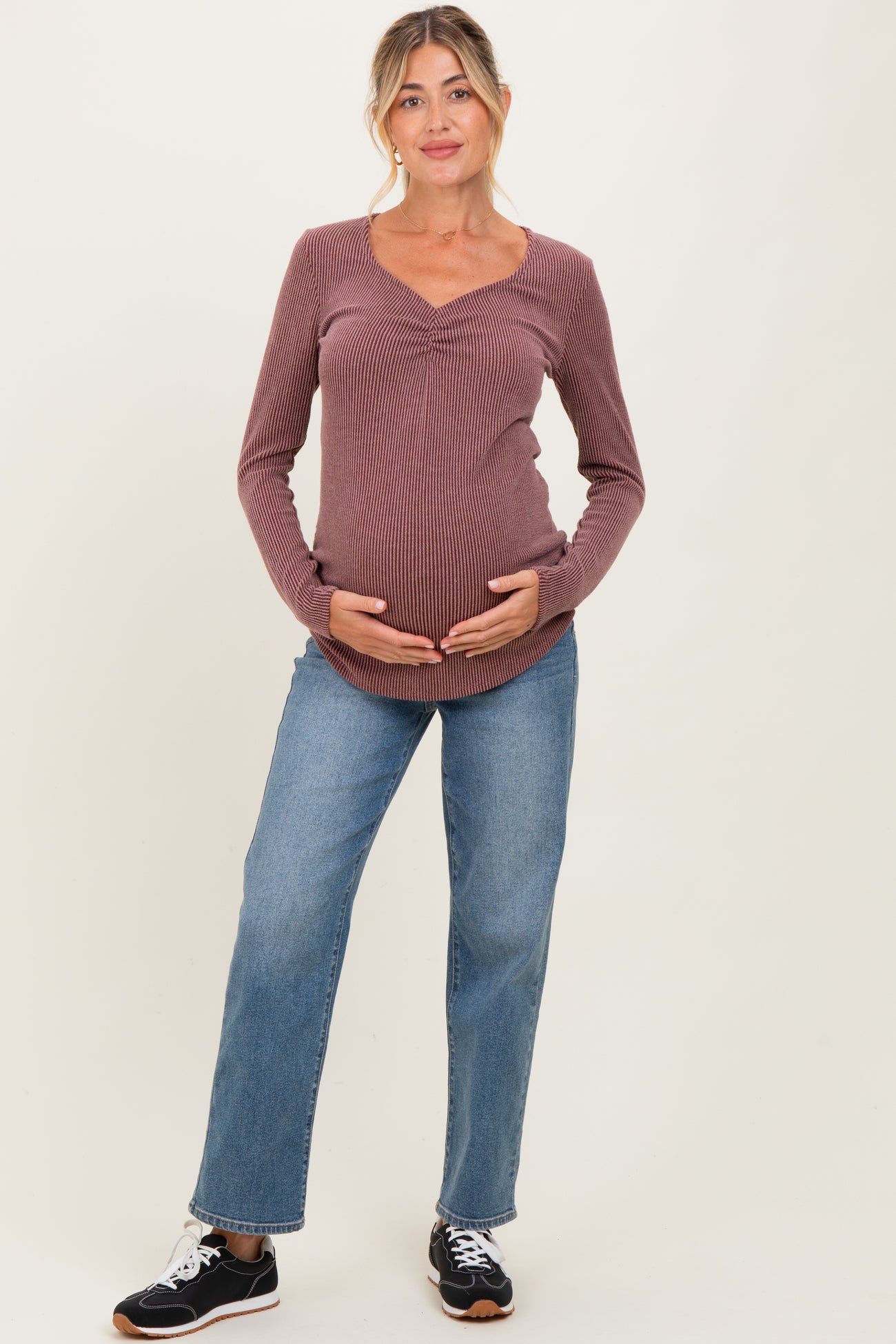 woman wearing a mauve ribbed long sleeve maternity top and blue jeans, holding her baby bump