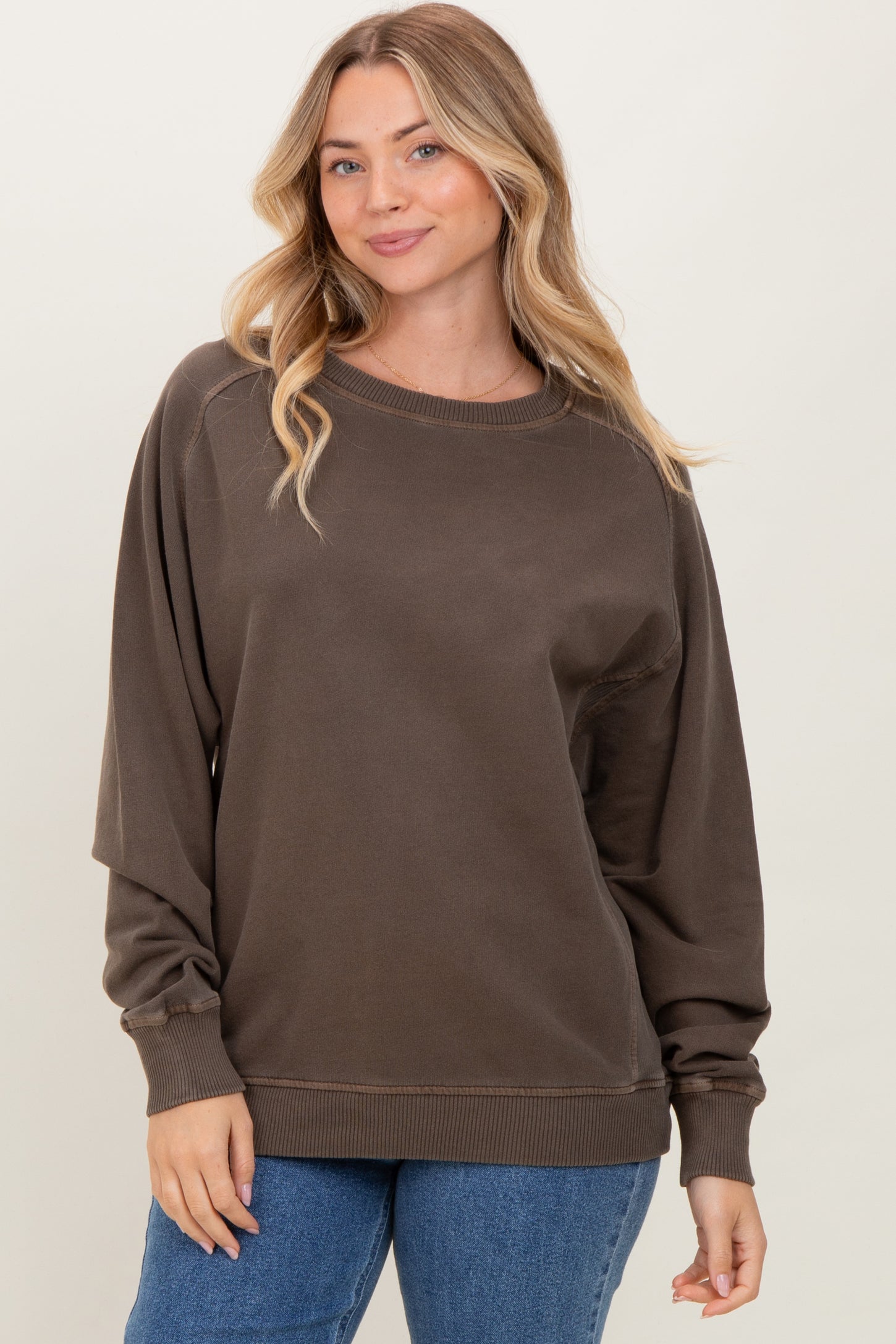 woman wearing a brown oversized sweatshirt with long sleeves and ribbed cuffs paired with blue jeans