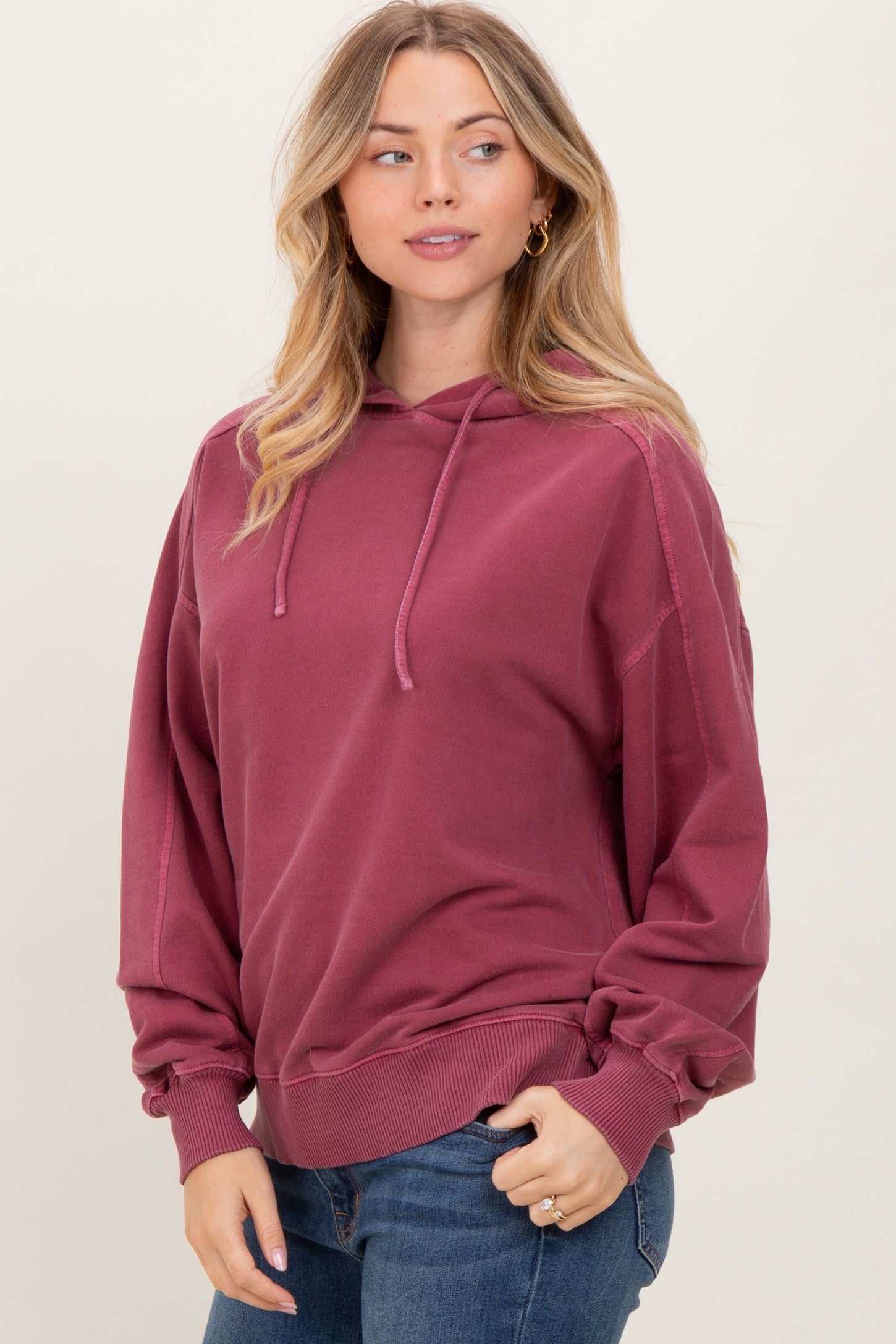 woman wearing a burgundy oversized hoodie with a front pocket and drawstring, paired with denim jeans