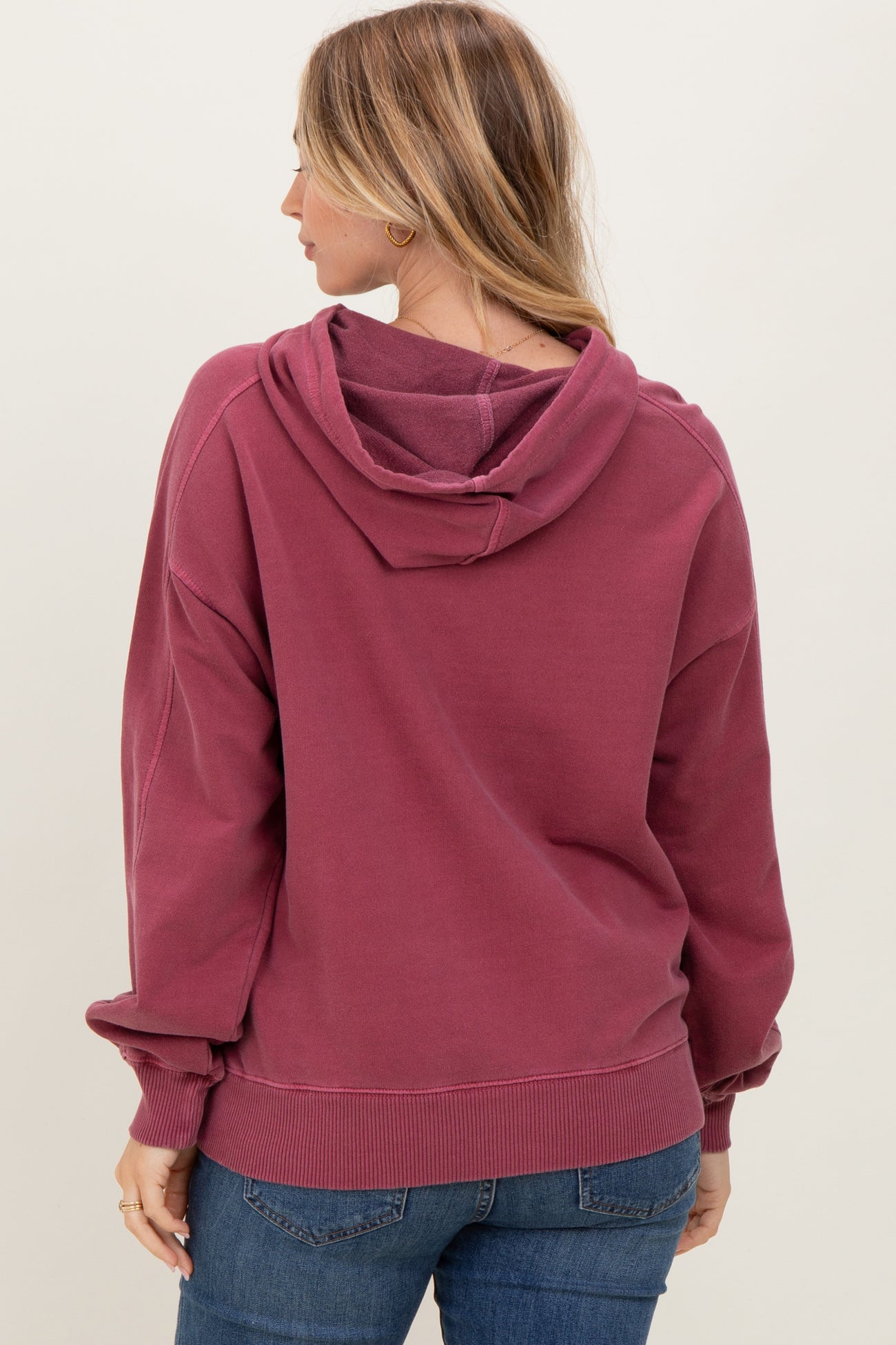 woman wearing a maroon oversized hoodie with a hood and ribbed cuffs, viewed from the back