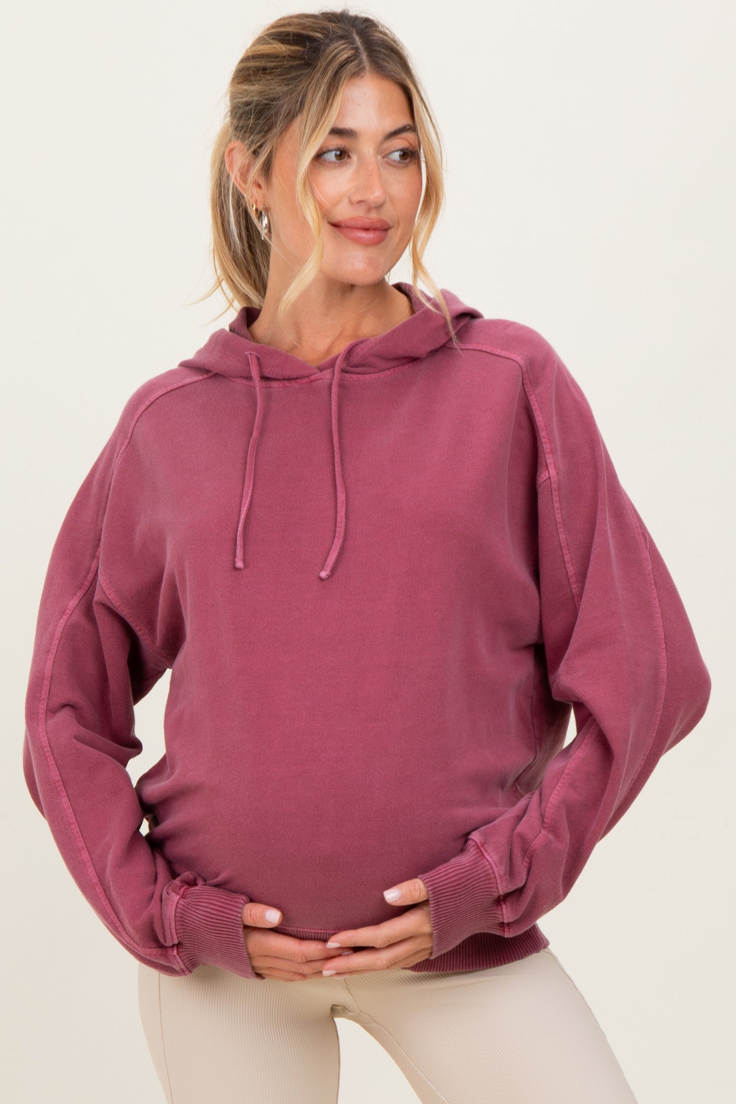 woman wearing a burgundy oversized maternity hoodie and holding her baby bump