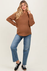 woman wearing a brown chunky knit maternity sweater and distressed blue jeans, showcasing her baby bump