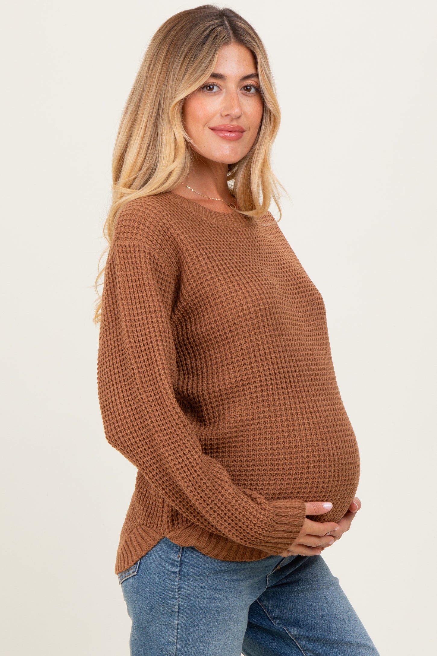 woman wearing a brown knitted maternity sweater and holding her baby bump