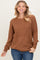 woman wearing a brown textured long sleeve sweater and blue jeans with a smile on her face