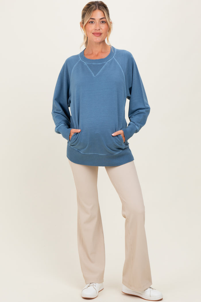 woman wearing a blue maternity sweatshirt with a relaxed fit and front pockets, paired with light beige pants and a baby bump visible
