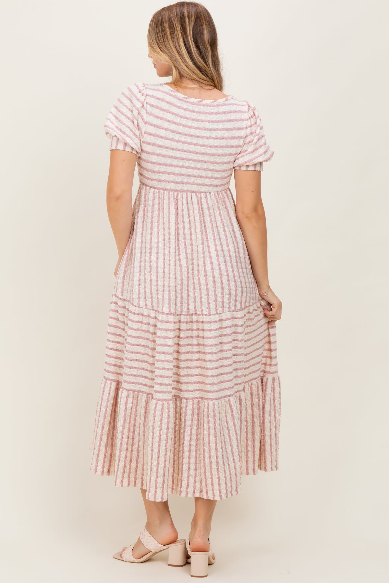 woman wearing a pink and white striped tiered maxi dress, showing the back view and short puff sleeves