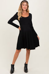 woman wearing a black long sleeve maternity dress with a tie at the waist and a visible baby bump