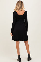 woman wearing a black long sleeve maternity dress with a scoop back and flared skirt style