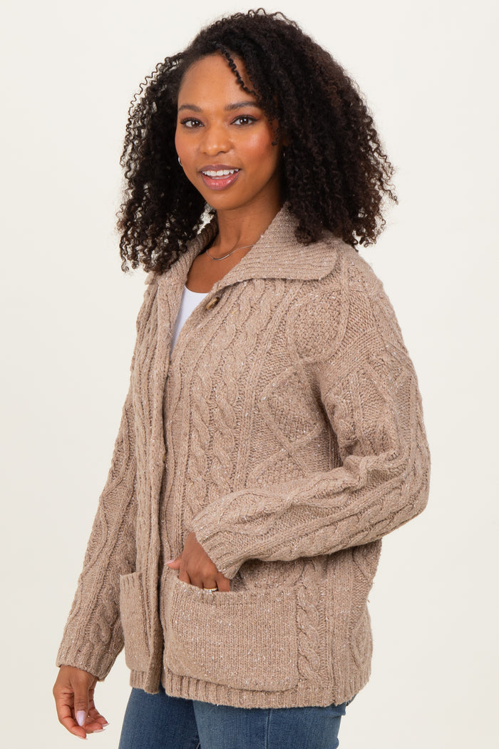 woman wearing a light brown cable knit cardigan with a collar and front pockets, smiling at the camera