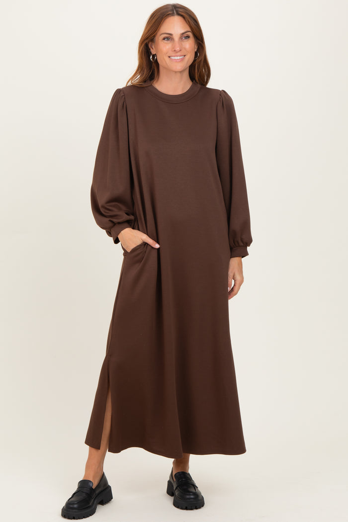 woman wearing a brown long sleeve maxi dress with puff sleeves and side pockets, standing and smiling