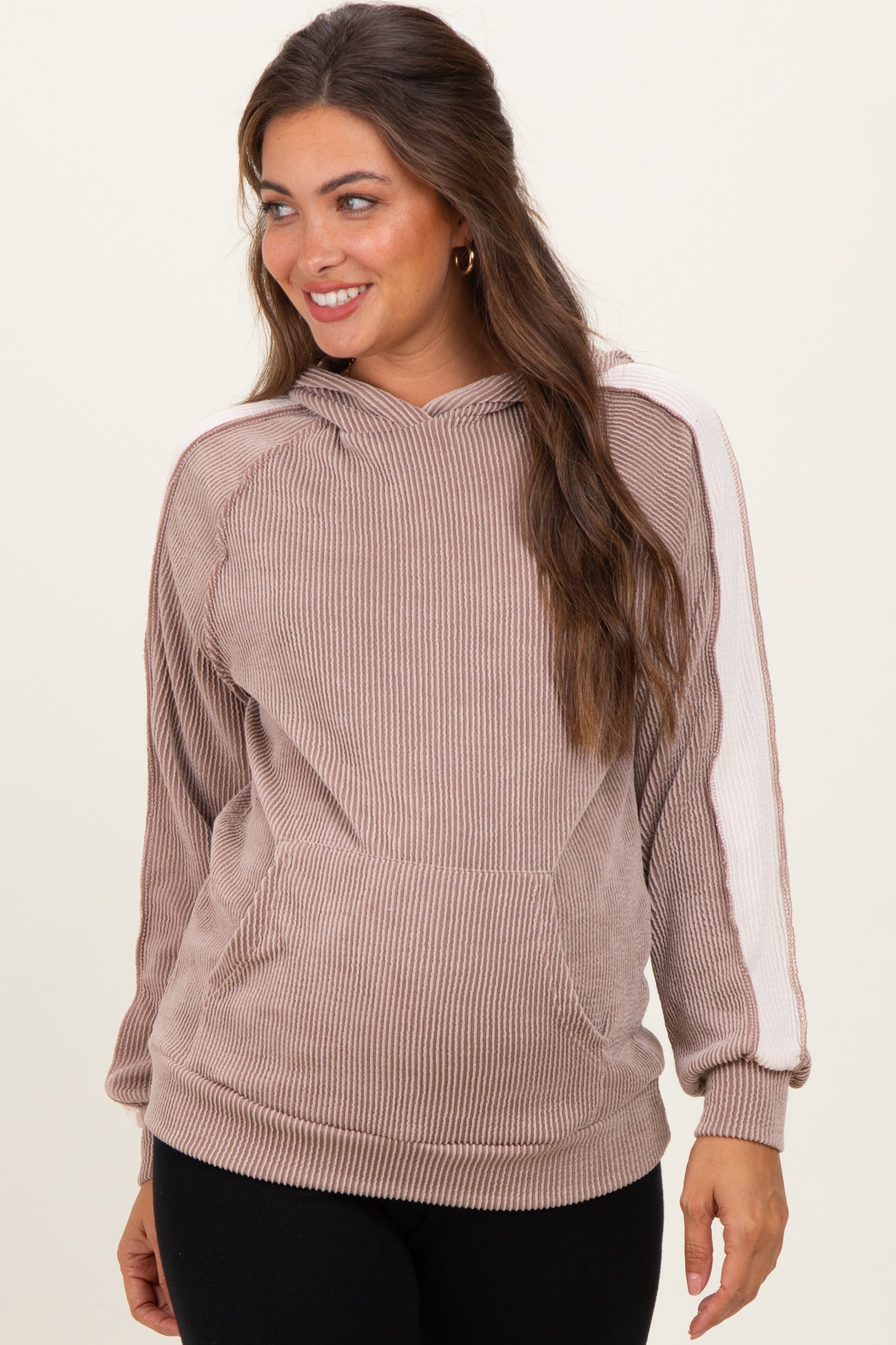 woman wearing a taupe maternity hoodie with a textured fabric and white side stripes, smiling and showing her baby bump