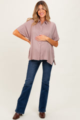 woman wearing a mauve short sleeve maternity button-up shirt and dark blue flared jeans, gently holding her baby bump