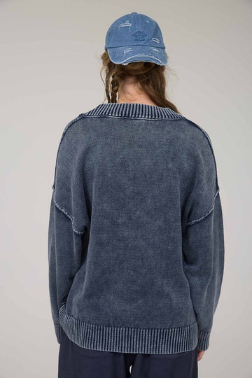 woman wearing a navy blue oversized sweater with a ribbed neckline and back details, styled with a casual cap