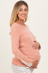 woman wearing a light peach maternity sweater with lace detail on sleeves and holding her baby bump