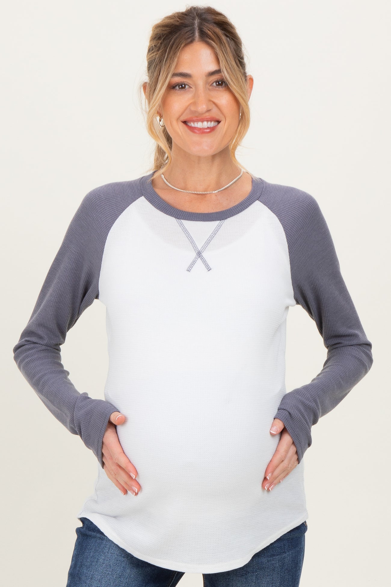 woman wearing a gray and white long sleeve maternity top and holding her baby bump