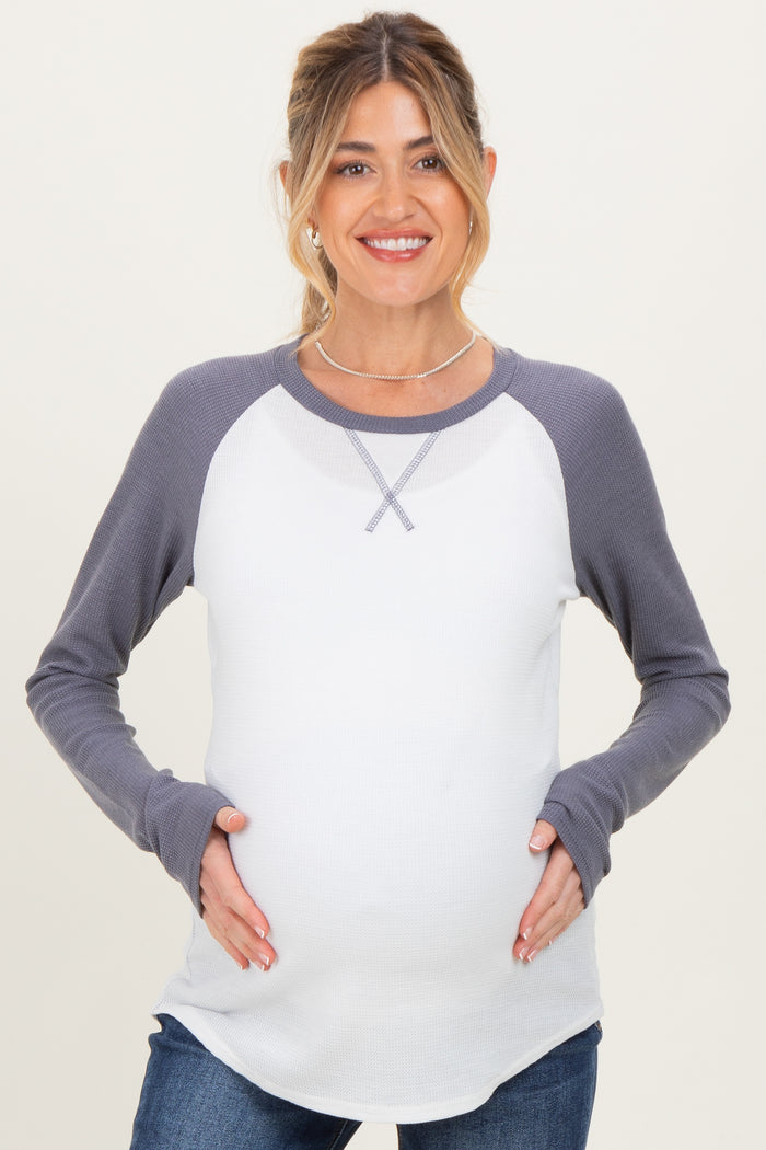 woman wearing a gray and white long sleeve maternity top and holding her baby bump