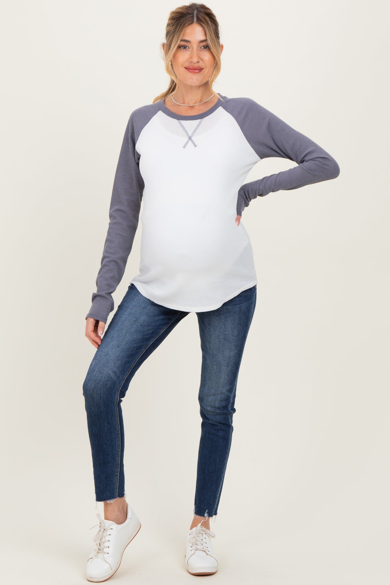 woman wearing a white and gray long sleeve maternity top with a baby bump and blue skinny jeans
