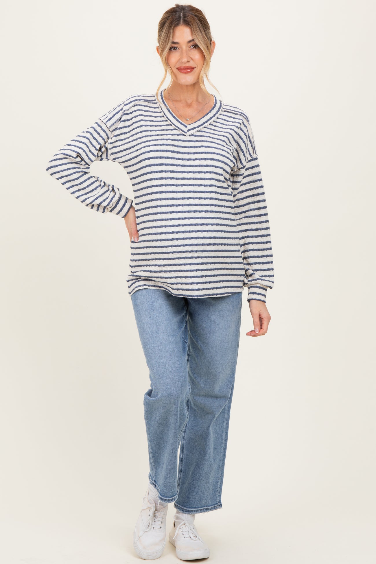 woman wearing a striped maternity sweater in navy and white with a v-neckline and blue jeans, showing her baby bump
