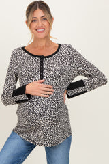woman wearing a beige leopard print maternity top with black trim, holding her baby bump and smiling