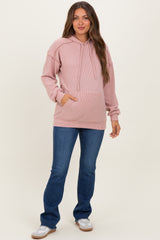 woman wearing a light pink ribbed maternity hoodie with a front pocket and blue flared jeans