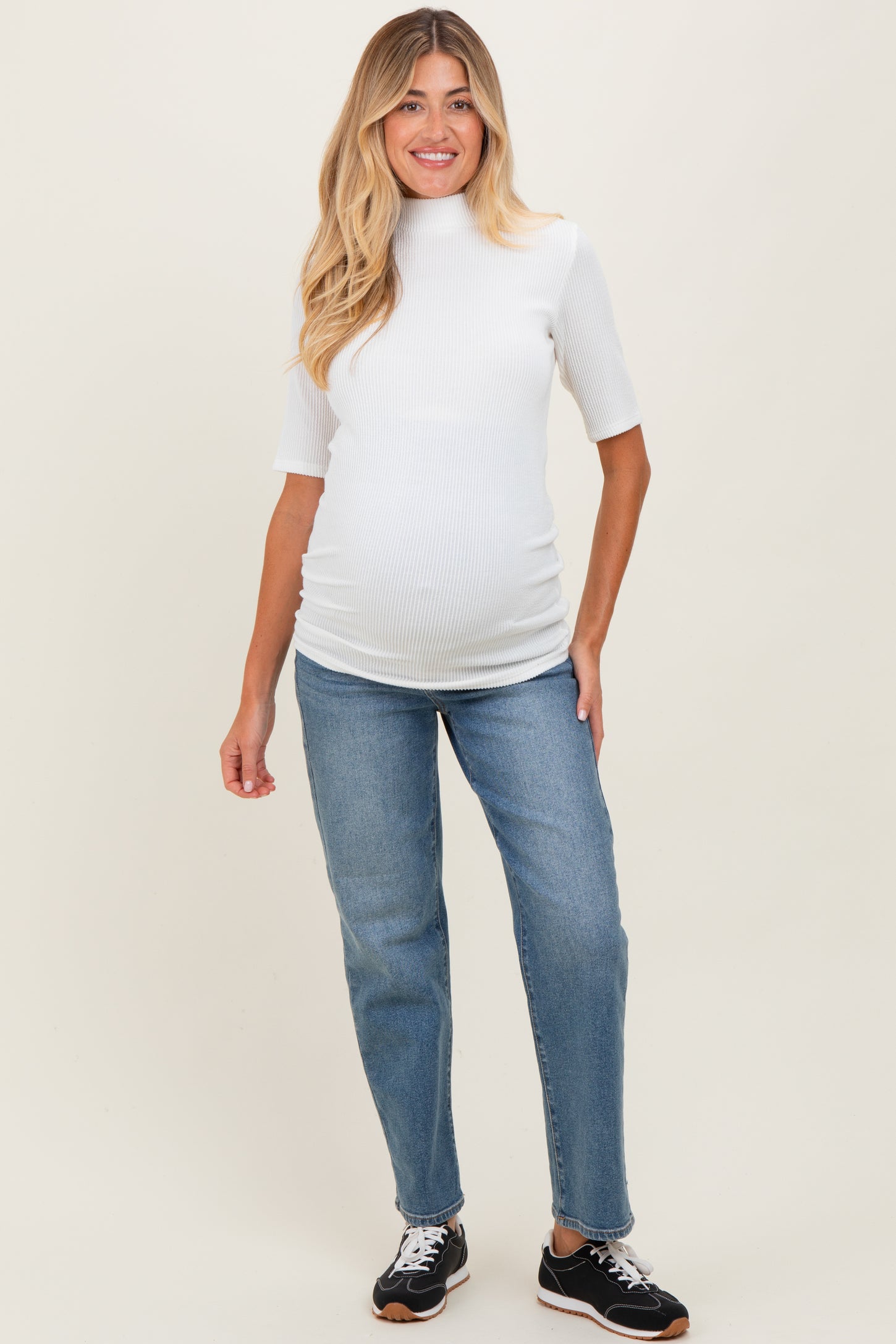 woman wearing a white ribbed maternity top and blue jeans, showing her baby bump