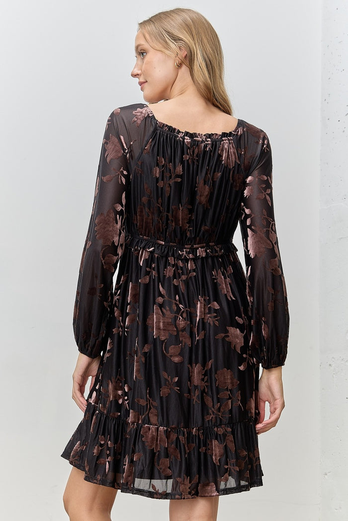woman wearing a black floral print dress with long sleeves and a tiered hem, view shows the back of the dress