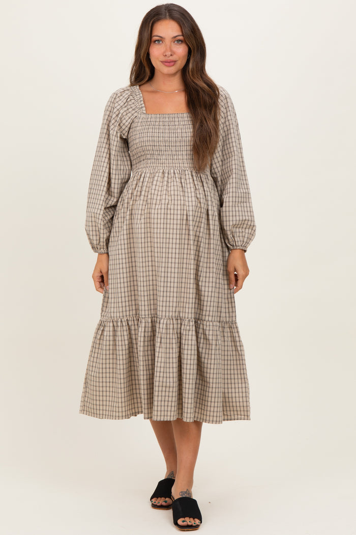 woman wearing a beige checkered maternity dress with puff sleeves and a tiered skirt, showcasing her baby bump