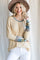 woman wearing a light yellow ribbed long sleeve top with patterned sleeves and a round neckline, smiling while holding her hat