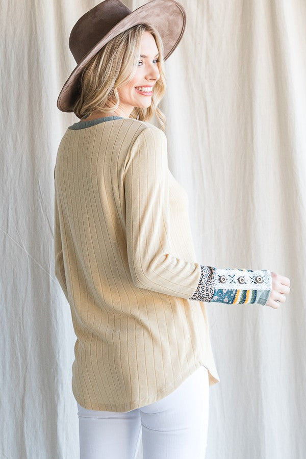 woman wearing a ribbed beige long sleeve top with patterned cuffs and a wide-brimmed hat, smiling and facing sideways