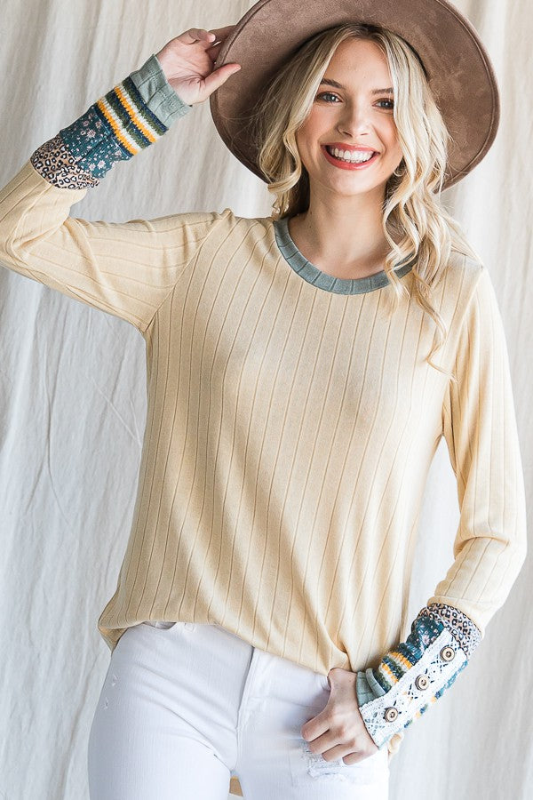 woman wearing a beige ribbed long sleeve top with patterned sleeves and a wide-brimmed hat, smiling at the camera