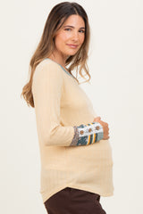 woman wearing a light beige maternity top with patterned long sleeves and holding her baby bump