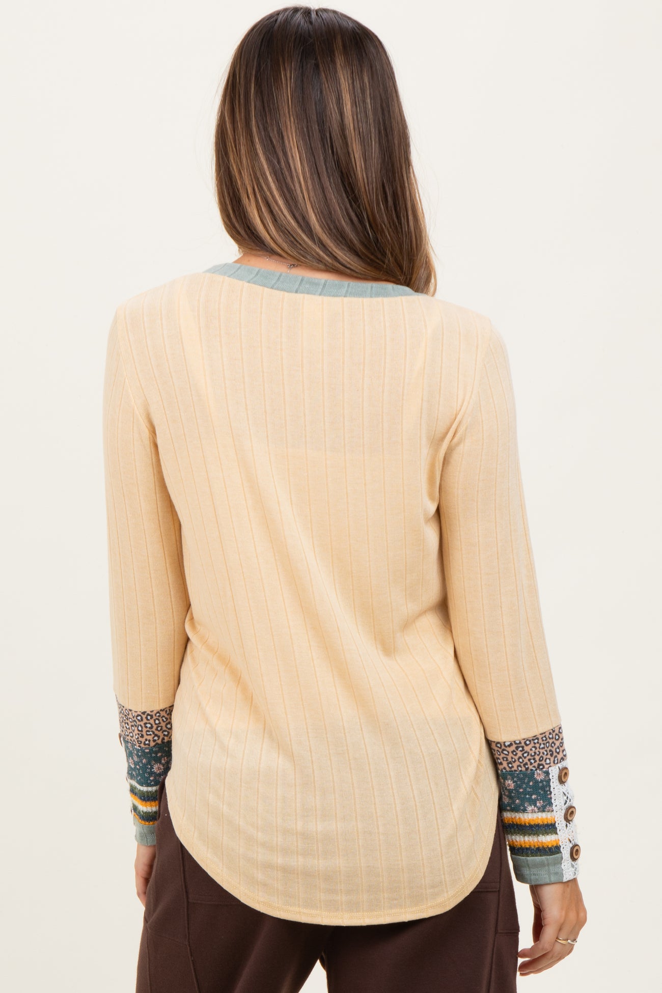 woman wearing a light beige maternity top with ribbed texture and patterned sleeves, showing the back view