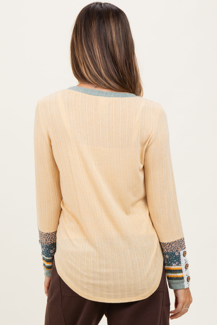 woman wearing a light beige maternity top with ribbed texture and patterned sleeves, showing the back view