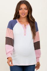 woman wearing a color-blocked maternity top with long sleeves and button details, showing a visible baby bump
