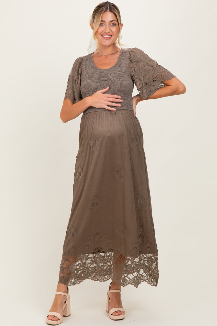 woman wearing a brown maternity dress with floral lace details, holding her baby bump