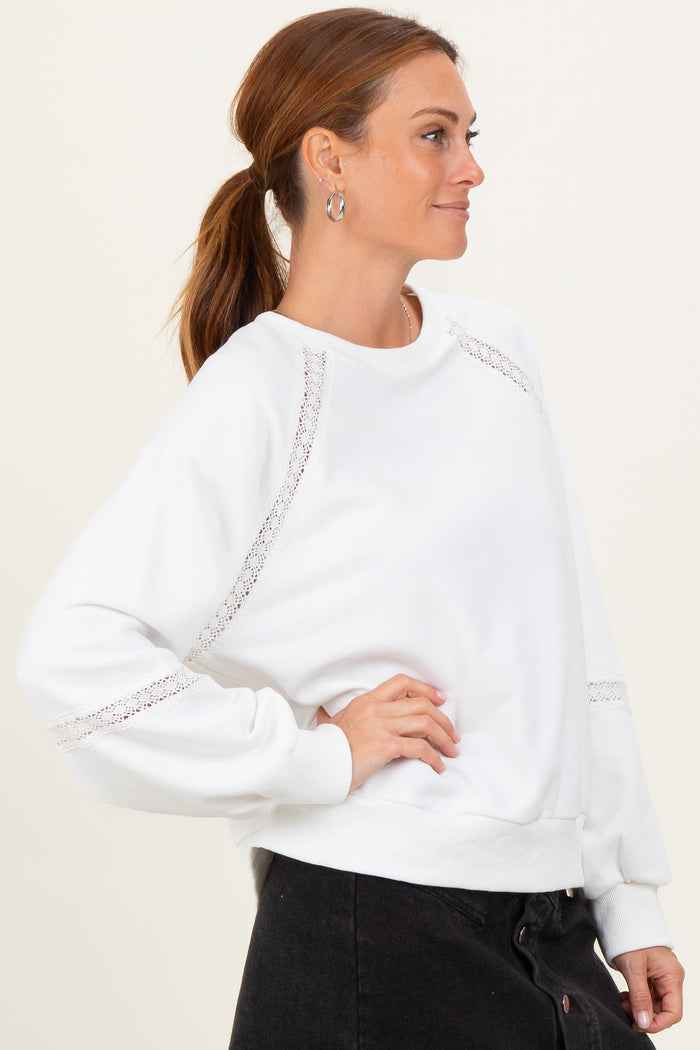 woman wearing a white sweatshirt with lace details on the sleeves and a relaxed fit