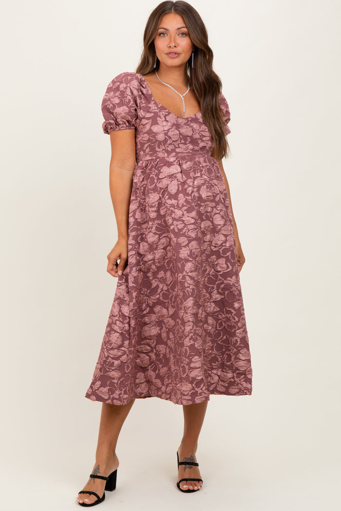 woman wearing a mauve floral maternity dress with puff sleeves and a flowy skirt, posing with a relaxed expression